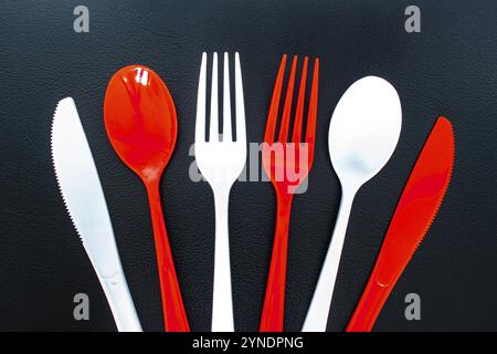 Single use red and white plastic cutlery on a leather background. Concept: Ban single use plastic Stock Photo