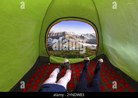 Two kids inside on a camping tent looking at the mountains during the day Stock Photo