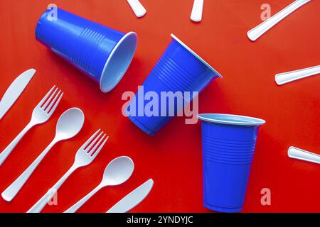 Single use white plastic cutlery and blue plastic glass on a red background. Concept: Ban single use plastic Stock Photo