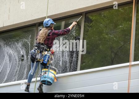 Calgary, Alberta, Canada. July 28, 2023. A female worker cleaning a window from a tall building during summer. Skyscraper Window Washer Stock Photo