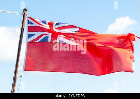 A fraying Red Ensign, or Red Duster flag flying in the breeze against a blue sky, Falmouth, UK Stock Photo