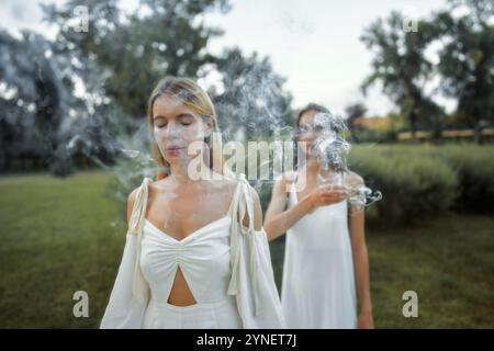 Two women in white dresses creating an ethereal atmosphere with smoke Stock Photo