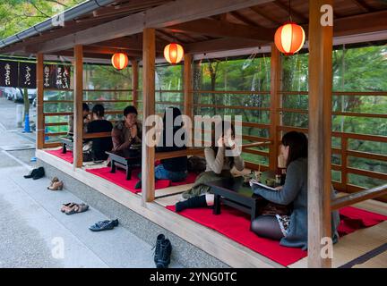 Visitors to Kiyomizu-dera Temple in Kyoto relaxing for an afternoon snack at low tables under a shelter with shoes removed. Stock Photo