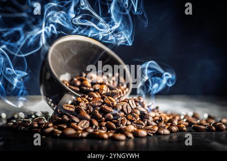 Roasted coffee beans in cup with smoke on a black table. Stock Photo