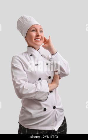 Female chef in white uniform looking up and touching her face, smiling and thinking about new recipes Stock Photo