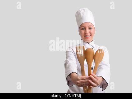 Professional female chef holding wooden kitchen utensils and smiling on white background Stock Photo
