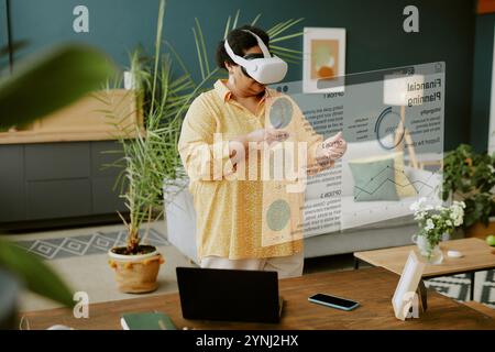 Senior African American woman with VR goggles studying VR business app while working remotely at home Stock Photo
