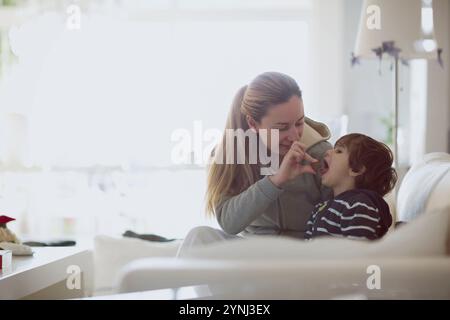 A mother plays with her young son in a cozy living room, sharing laughter and joy as they engage in a fun and loving interaction. The bright space add Stock Photo