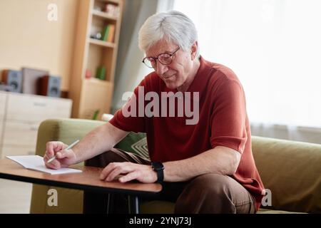 Portrait of white haired senior man smiling while writing music or poetry at home enjoying hobby in retirement Stock Photo