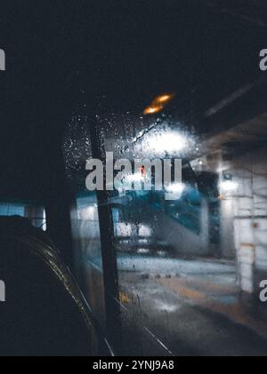 Moody Urban Scene Viewed Through Rain-Streaked Window at Night with Blurred City Lights and Reflections Stock Photo