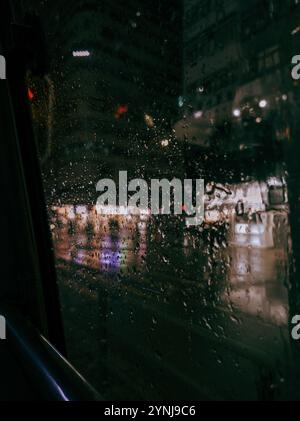 'Rain-Dappled Window Overlooking Blurred City Lights at Night, Capturing Urban Atmosphere and Reflections' Stock Photo