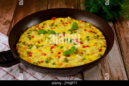 Colorful vegetable omelette cooking in black frying pan on rustic wooden table Stock Photo