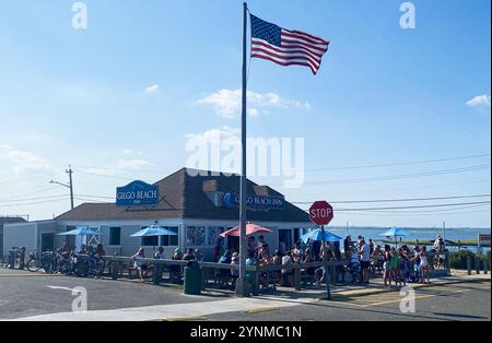 Gilgo Beach, NEw York, USA - August 2023: Patrons enjoy food and drinks outside at Gilgo Beach Bar while the American flag waves in the breeze. Stock Photo