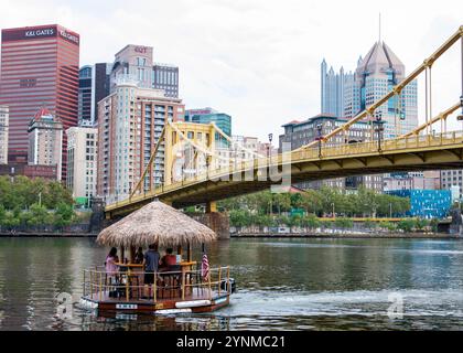 Pittsburgh, Pennsylvania, USA - 8 August 2023: A tiki bar sails on the river, showcasing Pittsburgh's skyline under a clear sky with vibrant building Stock Photo