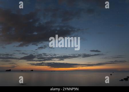 Night seascape, calm on the Baltic Sea, starry sky, on the horizon towards Finland the clouds are illuminated by the sun after sunset. Stock Photo