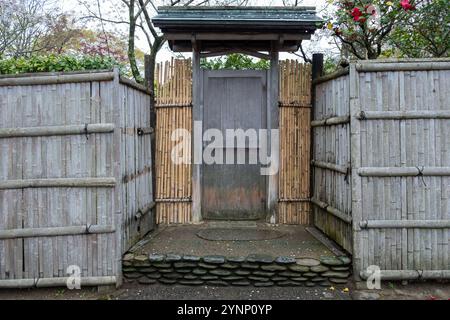 Traditional Japanese garden gate, a wooden door with a small roof framed by bamboo fences on both sides Stock Photo