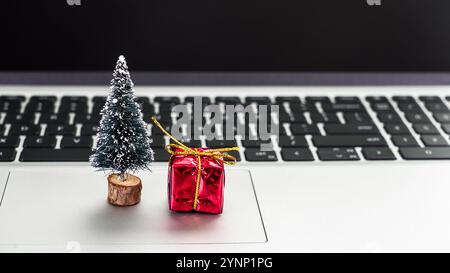 A small Christmas tree and a red gift sit on a laptop keyboard, capturing the festive spirit amid technology during the holidays. Stock Photo