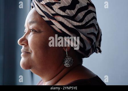 Minimal closeup portrait of Black senior woman wearing headscarf and smiling looking away in soft natural light accentuating profile Stock Photo