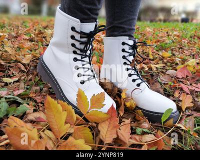 Autumn walk. Closeup of wonderful white boots on the fallen golden leaves. Fall concept. Beautiful modern white shoes with black laces Stock Photo