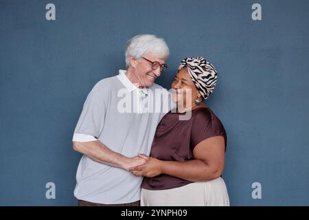 Minimal studio portrait of affectionate senior couple with Caucasian man and Black woman embracing gently and smiling against blue background Stock Photo
