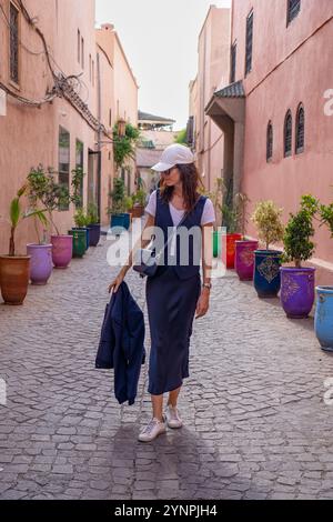 Young Dark Haired Woman Walking in Red Streets of Marrakech Surrounded by Colorful Pots, Morocco Stock Photo