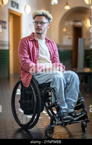 Man with disability in wheelchair in public hall, thoughtfully looking aside, thinking.  Stock Photo