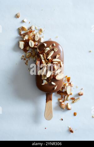 An almond ice cream stick covered with milk chocolate and sprinkled with roasted almonds on a white marble background Stock Photo