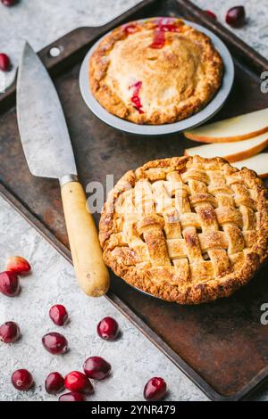 Two mini apple pies, both with golden brown crusts, rest on a rustic, weathered baking sheet on a gray countertop.  One pie has a lattice top and the Stock Photo