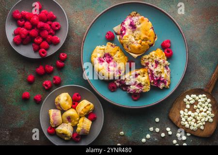 Freshly baked raspberry and white chocolate chip muffins on a teal ceramic plate,  scattered fresh raspberries and white chocolate chips on a custom b Stock Photo