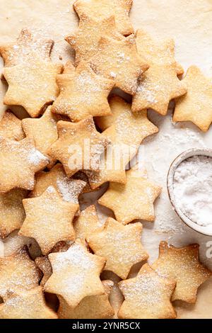Star-shaped shortcrust cookies dusted with a light sprinkle of powdered sugar. On the right side, a bowl filled with powdered sugar can be seen, used Stock Photo