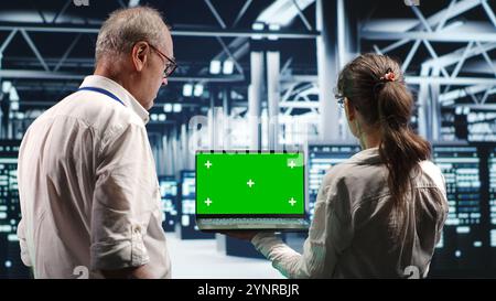 Admins using green screen laptop to monitor energy efficient data center clusters. Blade servers using renewable sources employed to minimize consumption and reduce overall location carbon footprint Stock Photo