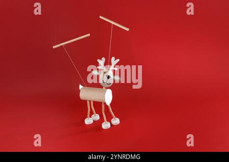 a handmade reindeer craft made from cardboard paper roll, bottle caps, marionette or hanging decoration. red background, DIY project that can be made Stock Photo