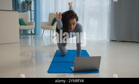 Yoga class with laptop workout video tutorial online training at home fit Caucasian woman sport trainer girl yogi female sportswoman doing exercise Stock Photo