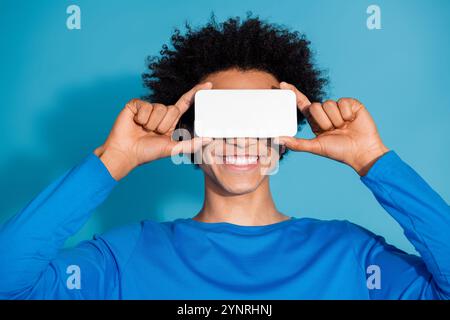 Photo portrait of pretty young male cover eyes white screen device wear trendy outfit isolated on blue color background Stock Photo