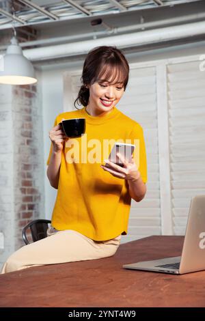 Woman in her 20s sitting at a desk operating a smartphone Stock Photo