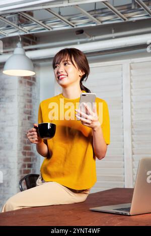 Woman in her 20s sitting at a desk operating a smartphone Stock Photo
