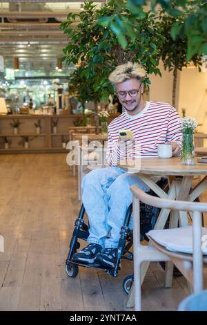 Smiling dreamy freelancer man drinking coffee at cafe table, using mobile phone. Coffee break. Stock Photo