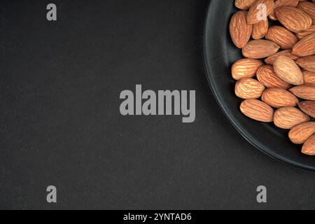 Almonds in black plate and Black Background, corner view, flat lay Stock Photo
