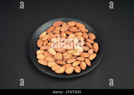 Fresh almonds in a black flat plate Stock Photo
