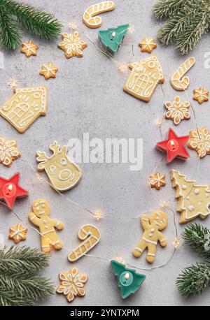 Christmas gingerbread cookies of various shapes surrounding lighted candles and pine branches on a gray background Stock Photo