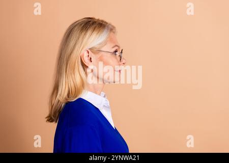 Elegant senior woman with blond hair and glasses in profile on beige background looking poised and professional Stock Photo