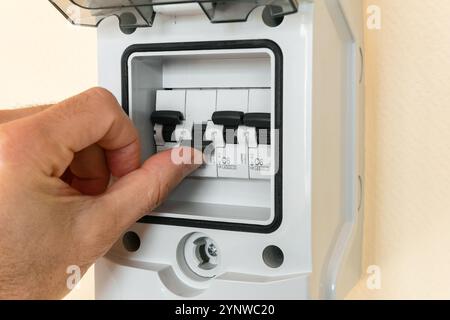 A man's hand turns on a disabled electrical circuit breaker. Stock Photo