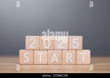 A businessman arranges wooden blocks spelling out 'START 2025' on a table, symbolizing the beginning of new goals and ventures for the upcoming year. Stock Photo