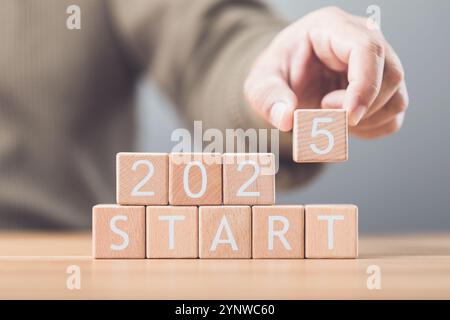 A businessman arranges wooden blocks spelling out 'START 2025' on a table, symbolizing the beginning of new goals and ventures for the upcoming year. Stock Photo