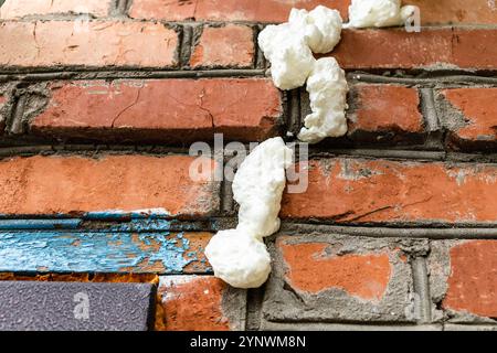 fresh construction foam filled cracks in brickwork in the wall of village barn close-up Stock Photo