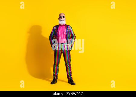 Photo of handsome senior man wear stylish striped bright suit hand hold in pockets isolated on yellow color background Stock Photo