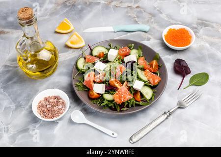 Salad with sliced salmon fish, white cheese feta, fresh tomato, cucumber, arugula, basil, spinach on the plate. Bowls with red caviar and salt, sliced Stock Photo