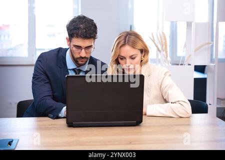 Business partners collaborating on laptop in modern office, smiling and working. Stock Photo