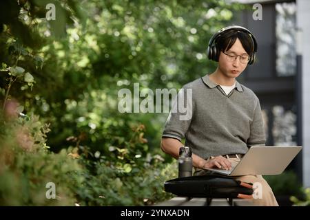 Medium shot of Asian male IT developer concentrated on using laptop to write code Stock Photo