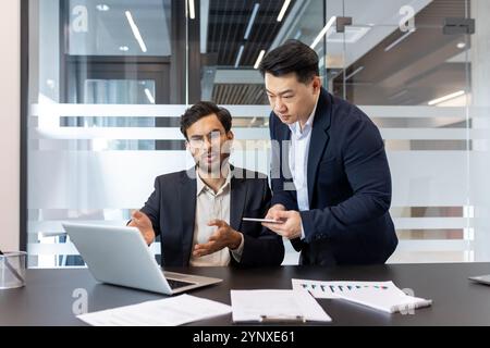 Two professionals in modern office collaborating on project, using laptop and smartphone. Discussing data for successful business outcomes and effective team collaboration. Stock Photo